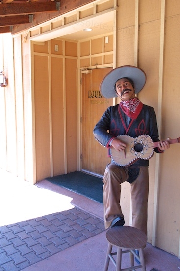 This vaquero is perched outside an unnamed cocktail lounge that has a for sale sign on the side wall.