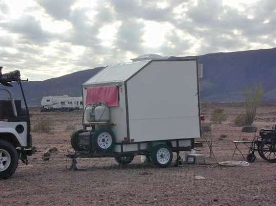 The front reveals a generator, propane, and spare tires. A towel over what appears to be a front window offers shading.