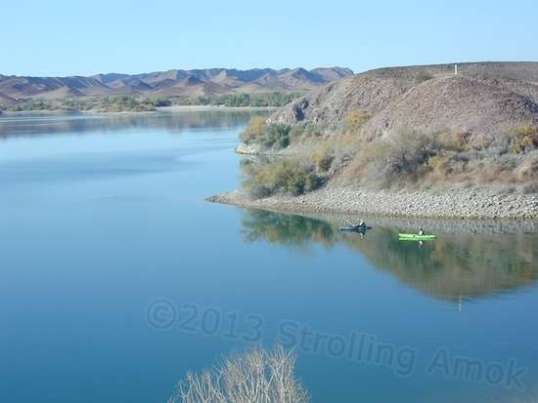 Two people fishing from kayaks in the reservoir while water levels are down.