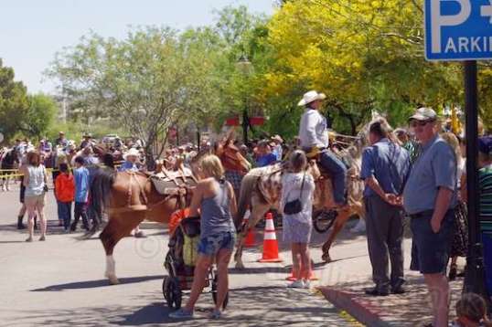 A crowd gathers in front of a small street stage off-camera left.