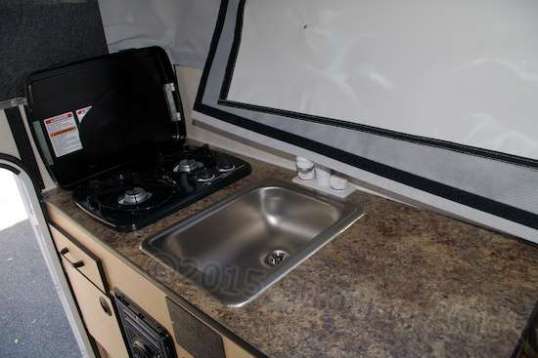 The obligatory shot of the driver's side counter, with sink and two-burner range top almost big enough to use. I'll be curious to find out if they bothered to connect the hot side to anything, since there's no water heater. As-is, it'll make a great spare source for parts, I guess. That black thing below is the furnace, and there's a silverware tray drawer, a good-sized cabinet, and the default battery bin in the same area.