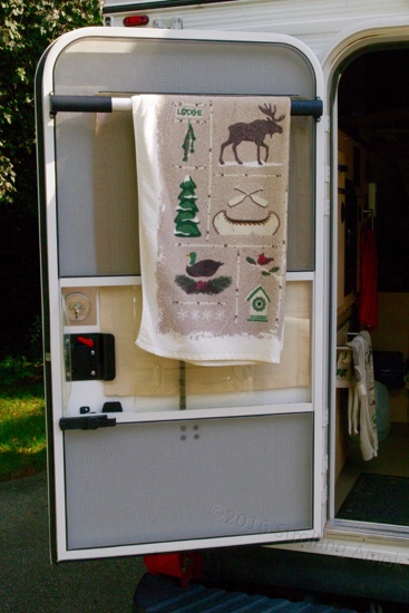 A Camco door bar doubles as a decent towel rack. I tried it with VHB tape to avoid drilling the door, but the grip surfaces are way too small. The screen door's very narrow frame makes accurate hole location important, and don't be ham-handed about torquing the screws down, either!